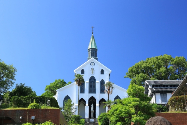 La fachada gótica blanca y la aguja verde de la iglesia de Ōura en Nagasaki bajo un cielo azul despejado